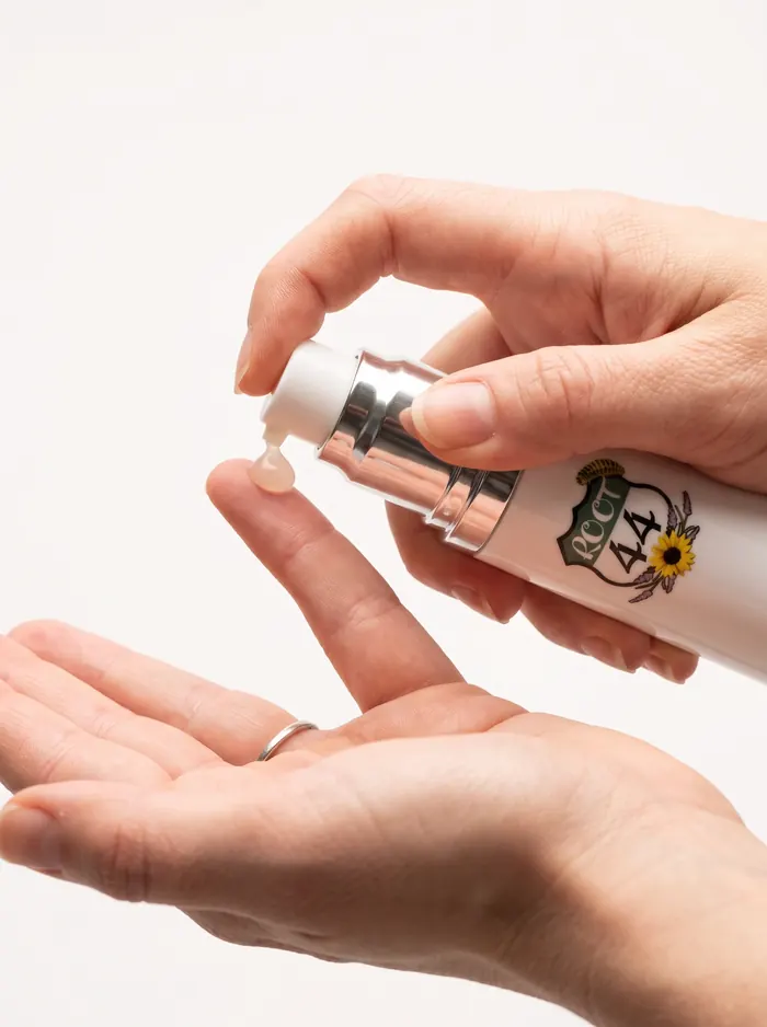 Hands pumping a drop of Root 44 Hyaluronic Serum onto a fingertip